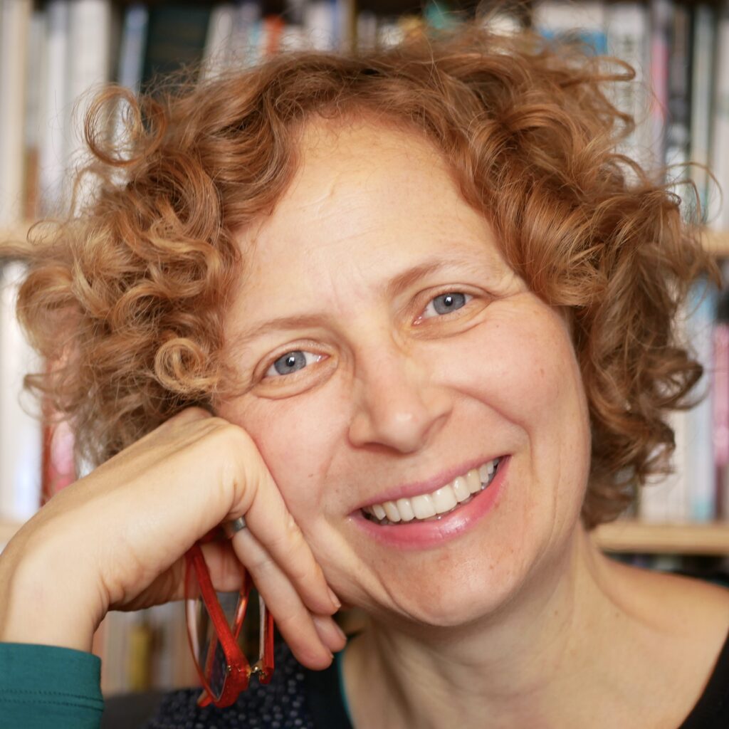 A photo of Alice Willitts' smiling face, leaning her head on her hand,